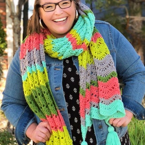 A vividly colored Calor Crochet Wrap by Marly Bird draped over a her, showcasing a wave crochet pattern and bright tassels.