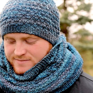 May include: A person wearing a blue and grey knitted hat and matching scarf. The hat and scarf are made of a soft, textured yarn.
