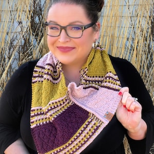 three color knit bandana cowl worn around the neck of Marly Bird. The bind off edge is seamed to the bottom ridge edge near the cast on to form a point in front when wearing it. The cowl is made in light pink, wine purple, and a golden wheat color.