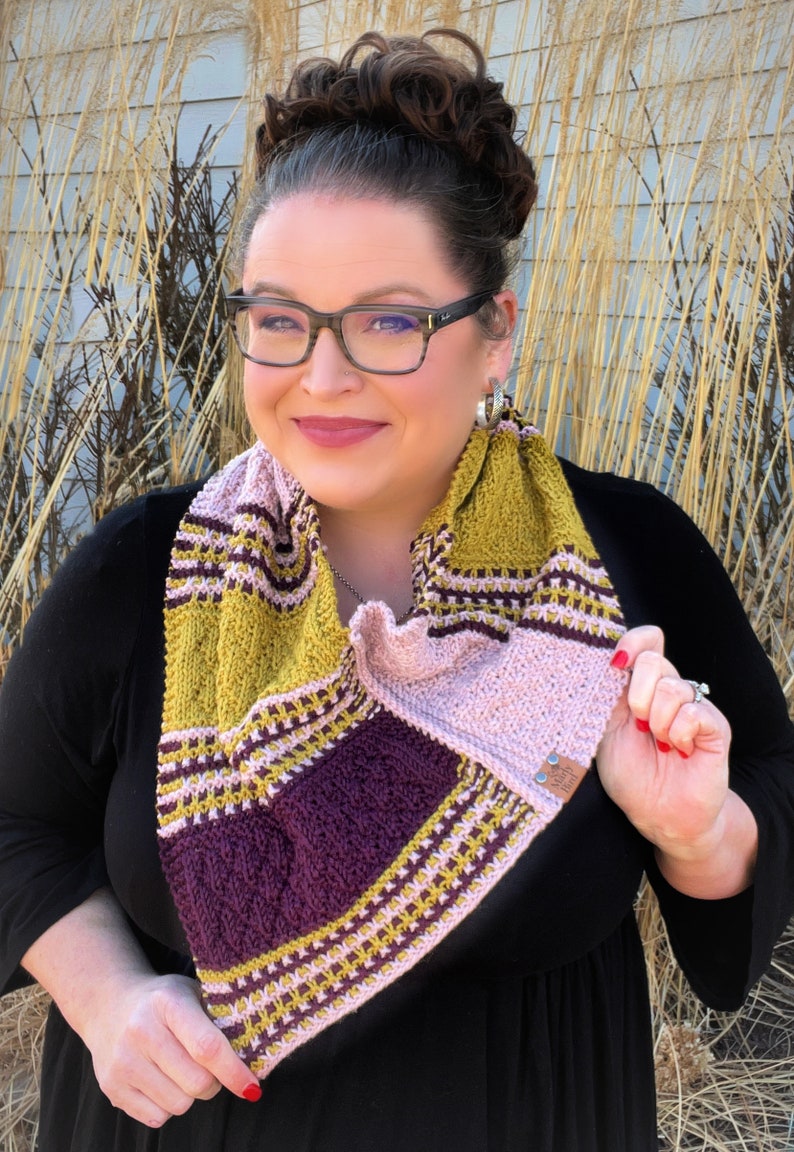 three color knit bandana cowl worn around the neck of Marly Bird. The bind off edge is seamed to the bottom ridge edge near the cast on to form a point in front when wearing it. The cowl is made in light pink, wine purple, and a golden wheat color.