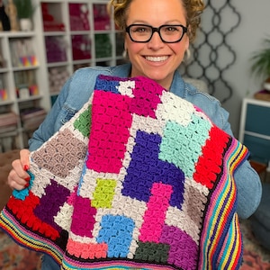 May include: A colorful, handmade crochet blanket featuring a patchwork design. The blanket showcases a vibrant mix of colors including pink, blue, green, purple, and red. The border is striped with rainbow hues. This cozy blanket is perfect for home decor.