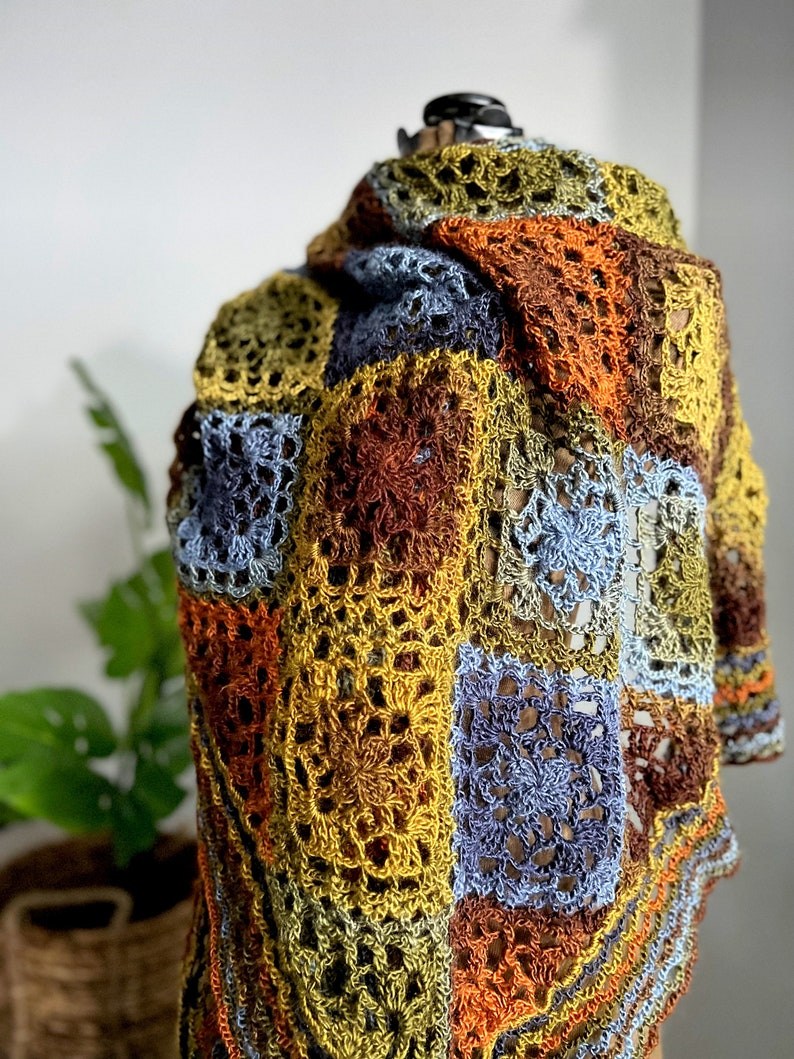 Handcrafted crochet shawl with earthy tones displayed on a model, showcasing intricate motifs in rich autumn color pallet. Enchanted Crochet Shawl by Marly Bird