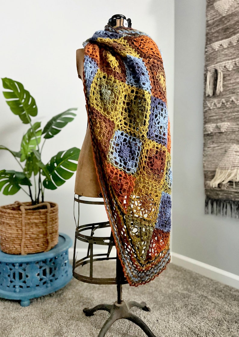 Handcrafted crochet shawl with earthy tones displayed on a model, showcasing intricate motifs in rich autumn color pallet. Enchanted Crochet Shawl by Marly Bird