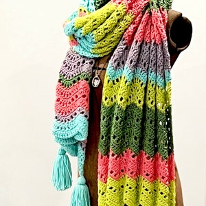 A vividly colored Calor Crochet Wrap by Marly Bird draped over a mannequin, showcasing a wave crochet pattern and bright tassels.