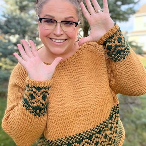 May include: A mustard yellow knitted sweater with green geometric patterns on the cuffs and hem.