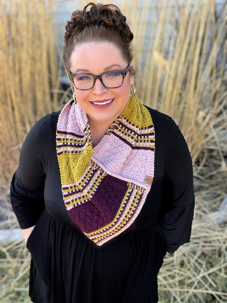 three color knit bandana cowl worn around the neck of Marly Bird. The bind off edge is seamed to the bottom ridge edge near the cast on to form a point in front when wearing it. The cowl is made in light pink, wine purple, and a golden wheat color.