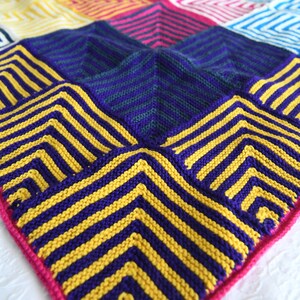 Steve Miter Knit Throw Blanket, artfully spread to showcase its vivid pattern of mitered squares in a spectrum of colors such as purple, blue, yellow, red, and pink. The garter stitch texture adds depth to the bold, geometric design. marly bird