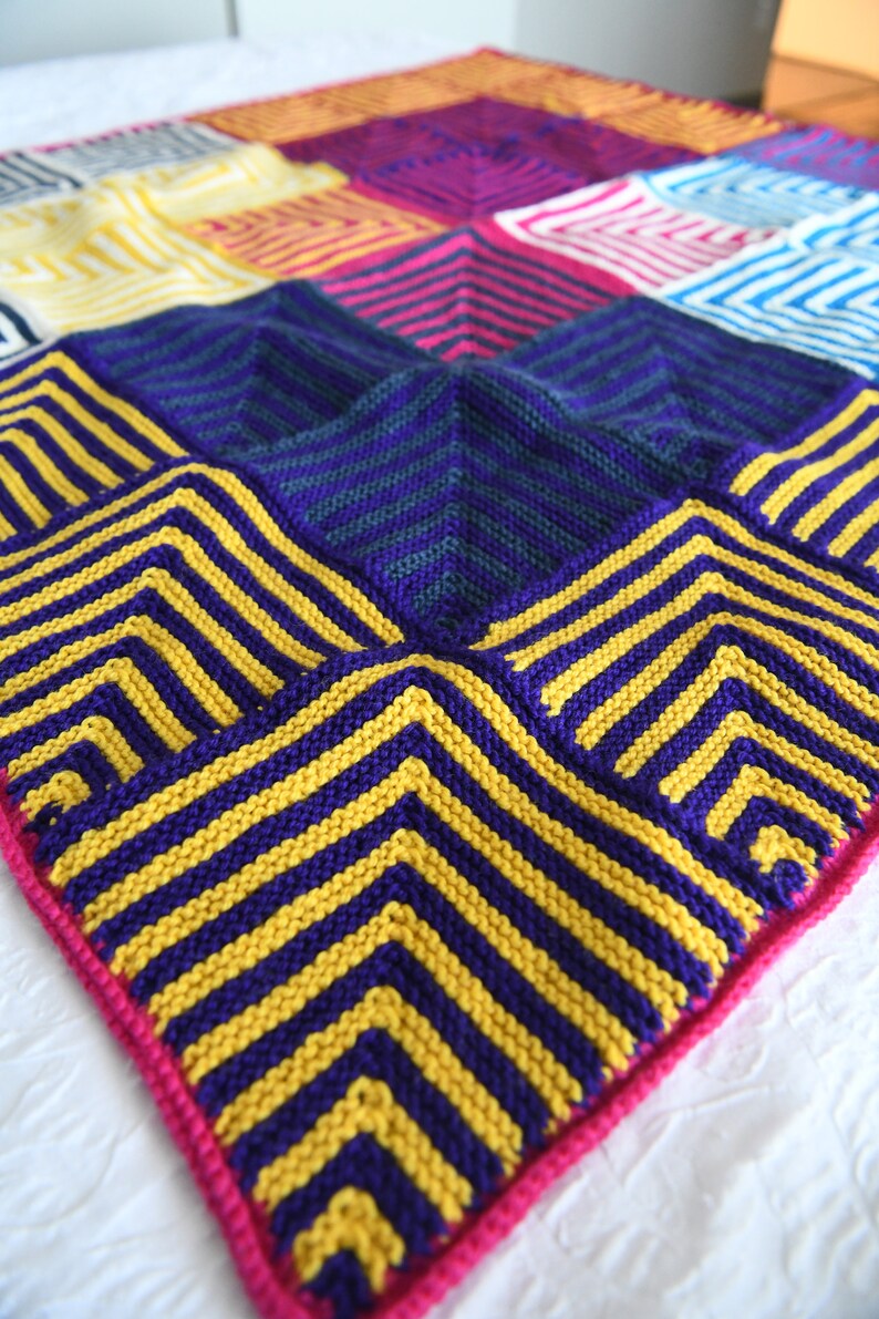 Steve Miter Knit Throw Blanket, artfully spread to showcase its vivid pattern of mitered squares in a spectrum of colors such as purple, blue, yellow, red, and pink. The garter stitch texture adds depth to the bold, geometric design. marly bird