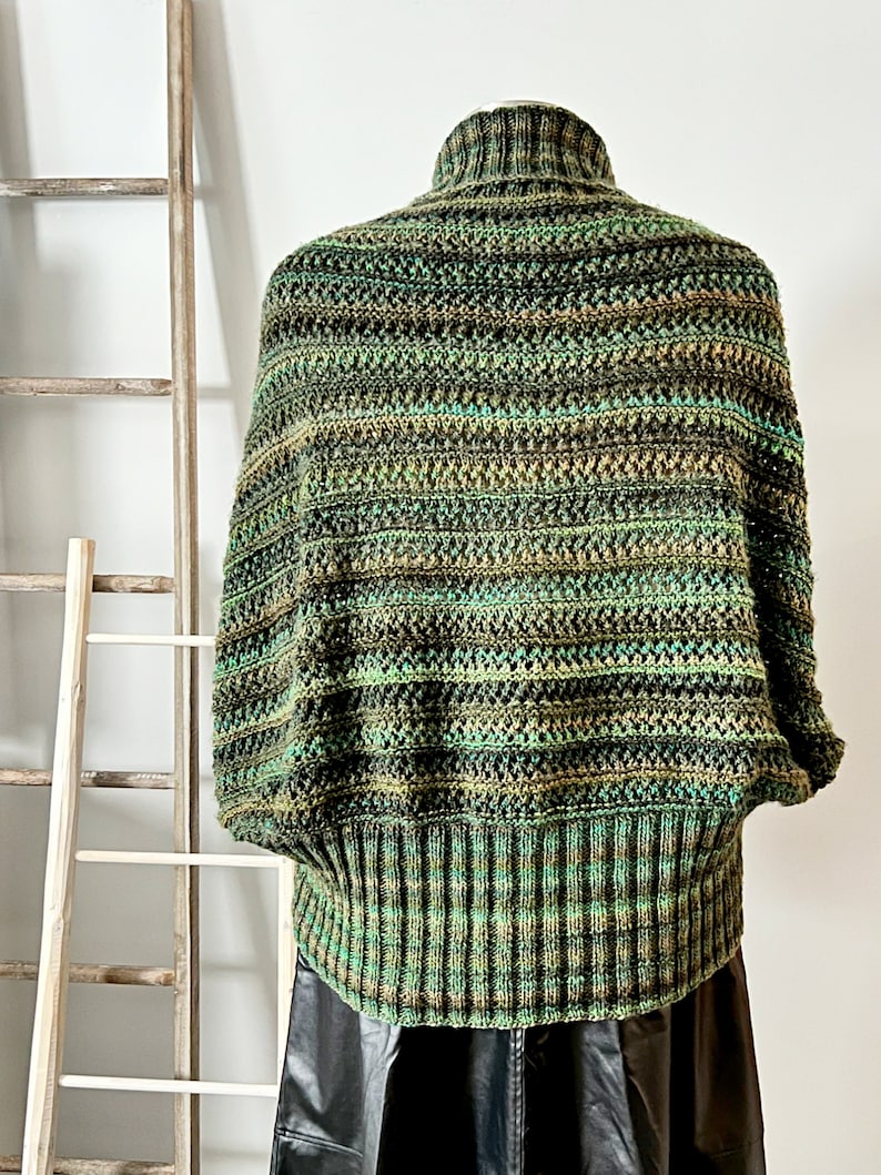 An elegantly draped, hand-knit cocoon cardigan displayed on a mannequin, showcasing rich hues of green with a subtle variegated pattern, chunky ribbed collar, and a large decorative button at the front. Marly Bird Know Your Worth Knit Cocoon Cardigan