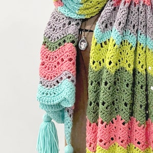 A vividly colored Calor Crochet Wrap by Marly Bird draped over a mannequin, showcasing a wave crochet pattern and bright tassels.