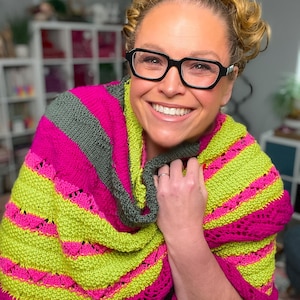 May include: A vibrant, hand-knitted shawl in shades of neon green, hot pink, and gray. The shawl features a striped pattern with intricate lace detailing along the edges. The soft, textured yarn creates a cozy and stylish accessory.