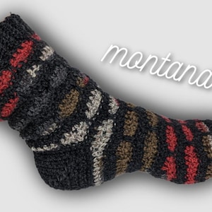 May include: A single, hand-knitted sock in a dark color palette. The sock features a textured pattern with accents of red, brown, and off-white. The word "montana" is written in cursive across the image. This cozy sock is perfect for cold weather.