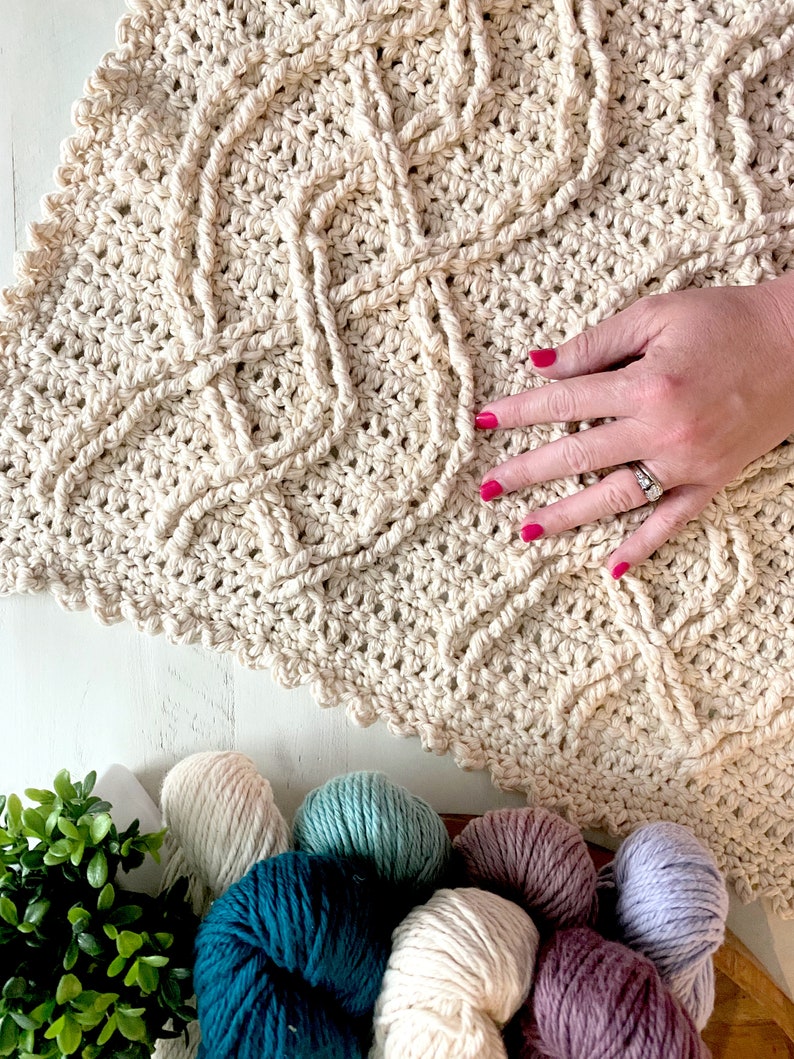 A crochet project in progress with a beautiful textured pattern, surrounded by skeins of colorful yarn and crochet tools, evoking a sense of creativity and craftsmanship for a unique handmade gift. Inishmore Crochet Cable Blanket - Marly Bird