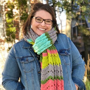 A vividly colored Calor Crochet Wrap by Marly Bird draped over a her, showcasing a wave crochet pattern and bright tassels.