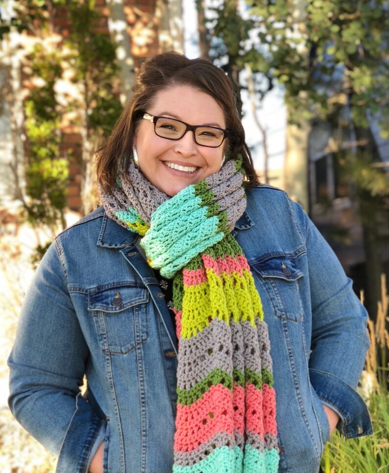A vividly colored Calor Crochet Wrap by Marly Bird draped over a her, showcasing a wave crochet pattern and bright tassels.