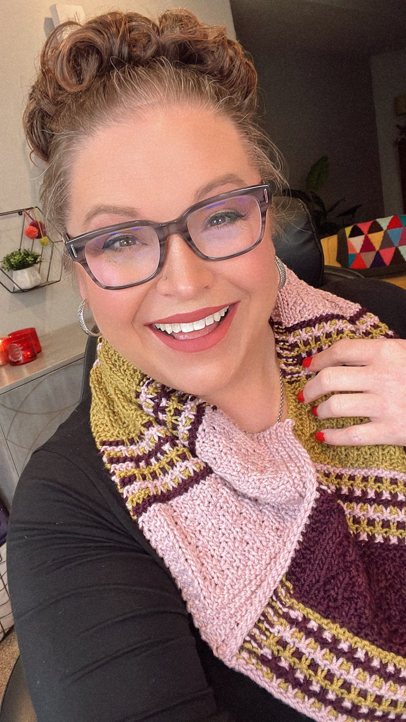 three color knit bandana cowl worn around the neck of Marly Bird. The bind off edge is seamed to the bottom ridge edge near the cast on to form a point in front when wearing it. The cowl is made in light pink, wine purple, and a golden wheat color.