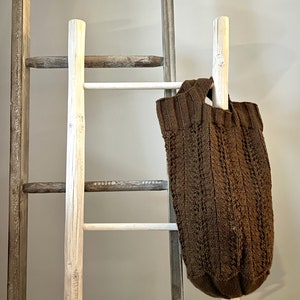 Brown knit market bag hanging from a wood ladder resting against the wall. Pattern by marly Bird