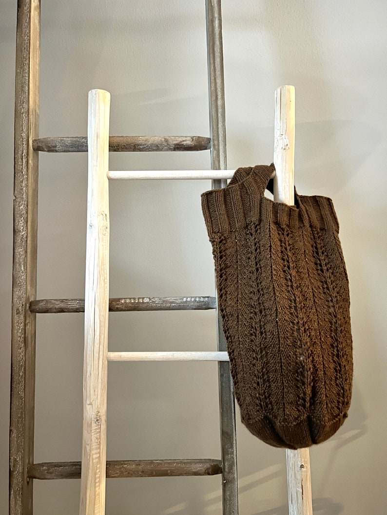 Brown knit market bag hanging from a wood ladder resting against the wall. Pattern by marly Bird