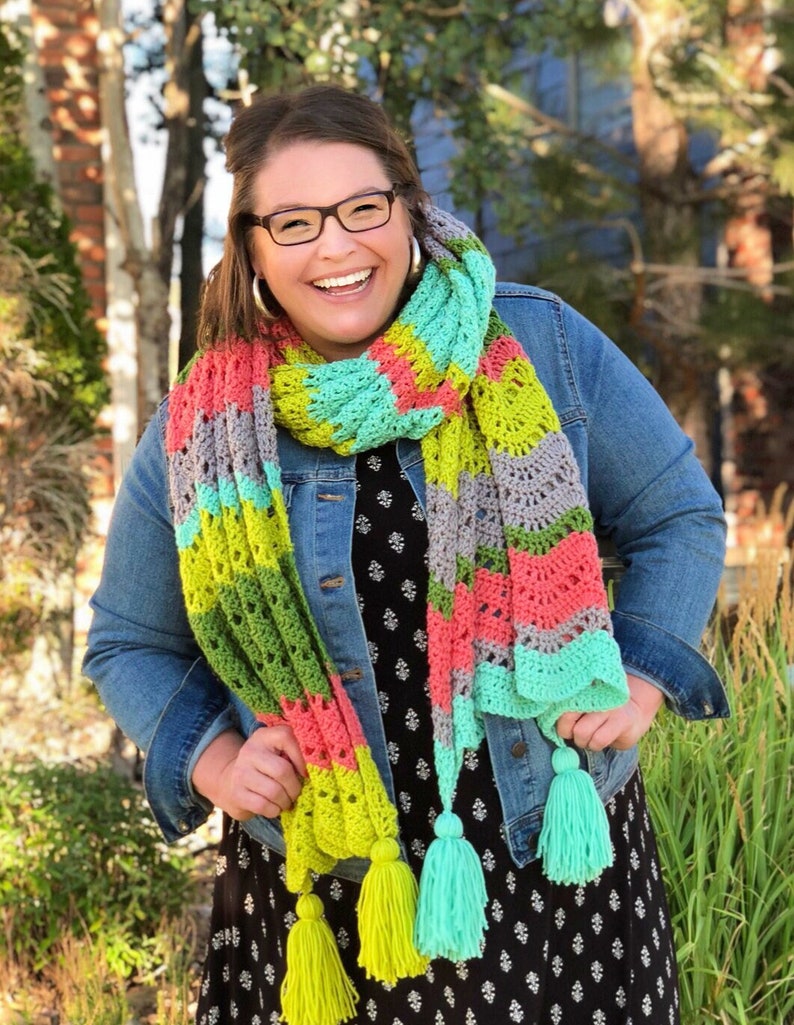 A vividly colored Calor Crochet Wrap by Marly Bird draped over a her, showcasing a wave crochet pattern and bright tassels.