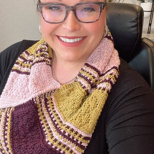 three color knit bandana cowl worn around the neck of Marly Bird. The bind off edge is seamed to the bottom ridge edge near the cast on to form a point in front when wearing it. The cowl is made in light pink, wine purple, and a golden wheat color.