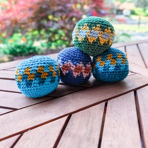 Puede incluir: Cuatro bolas de ganchillo esféricas dispuestas en una pila. Las bolas presentan intrincados patrones de hilo en tonos azul claro, azul oscuro, verde, amarillo y rosa. Cada bola está elaborada con un punto apretado y uniforme.