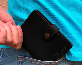 May include: A black leather wallet with a brown snap closure and stitching. The wallet is partially visible in a blue jeans pocket. The word "Veloure" is embossed on the wallet.