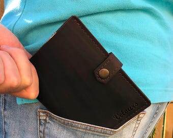 May include: Dark brown leather wallet with a snap closure and the word "Velours" embossed on the front. The wallet is partially visible in a back pocket of blue jeans.