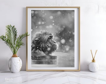 May include: Black and white framed print of a Japanese macaque, also known as a snow monkey, in a hot spring. The monkey is partially submerged in water, with snowflakes falling around it. The print is displayed on a white marble surface.