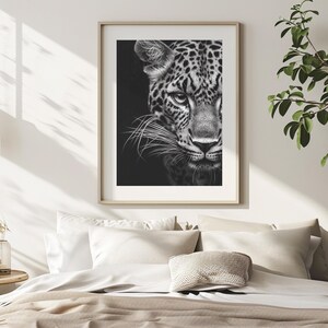 Peut inclure: Photographie en noir et blanc d'un visage de l&eacute;opard. L'image est encadr&eacute;e et accroch&eacute;e &agrave; un mur blanc au-dessus d'un lit avec une literie blanche et un coussin.