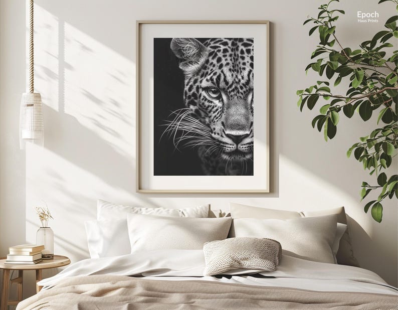 Peut inclure: Photographie en noir et blanc d'un visage de l&eacute;opard. L'image est encadr&eacute;e et accroch&eacute;e &agrave; un mur blanc au-dessus d'un lit avec une literie blanche et un coussin.