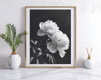 May include: Black and white framed print featuring two large peony flowers. The flowers are in full bloom, with delicate petals and lush green leaves. The print is in a gold frame, and the overall aesthetic is elegant and timeless.