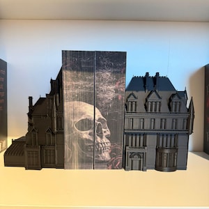 Könnte beinhalten: Ein Paar schwarze Buchstützen in Form eines gotischen Herrenhauses mit einem Totenkopf- und Rosendesign auf der mittleren Buchstütze.