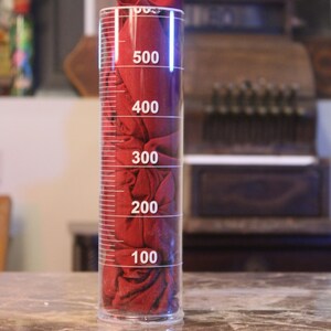 May include: A clear glass graduated cylinder with a red fabric inside. The cylinder has markings for 100, 200, 300, 400, and 500.