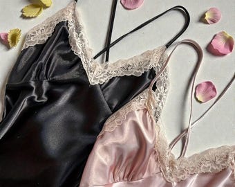 May include: Two satin camisoles, one black and one blush pink, with delicate lace trim. The camisoles have thin straps and are adorned with pink rose petals and yellow flower petals.