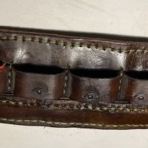 May include: A brown leather belt with eight loops for holding cartridges. The belt is stitched with white thread and has a worn look.
