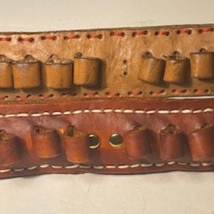 May include: Two leather gun belts with multiple loops for bullets. The top belt is light brown with red stitching and the bottom belt is dark brown with white stitching.