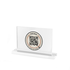 May include: A clear acrylic rectangular sign holder with a base, featuring a circular graphic with a QR code in the center. The graphic includes the text MENU and Scan to order, along with small icons of a fork, knife, and a plate.