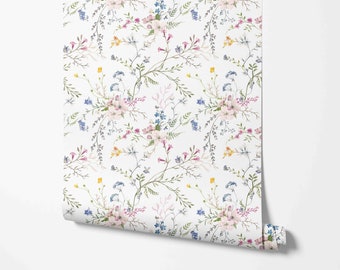 May include: A roll of wallpaper featuring a delicate floral pattern. The design includes clusters of pink, blue, and yellow flowers with green foliage on a white background. The wallpaper is partially unrolled, revealing the pattern.