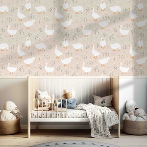 Op de afbeelding: Een babykamer met een wit wiegje en een wit en roze behang met een herhalend patroon van witte ganzen. Het behang heeft een subtiel bloemenpatroon met kleine witte bloemetjes.