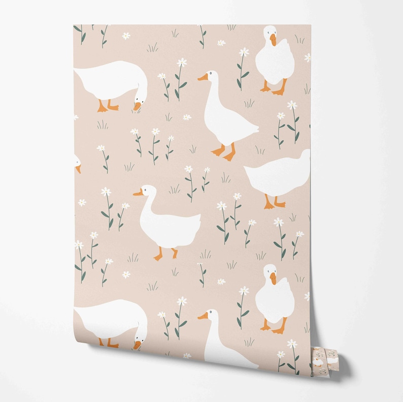 Op de afbeelding: Een naadloos patroon met witte ganzen met oranje snavels en poten op een lichtroze achtergrond met groen gebladerte en witte bloemen.