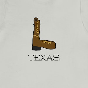 May include: A light gray t-shirt with a brown cowboy boot graphic and the word "TEXAS" printed in black below the boot.