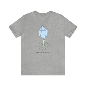 以下が含まれることがあります： ヘザーグレーのTシャツに、バクテリアに感染するウイルスであるバクテリオファージの漫画イラストが描かれています。イラストの下には「DOWNLOAD COMPLETE」というテキストが印刷されています。