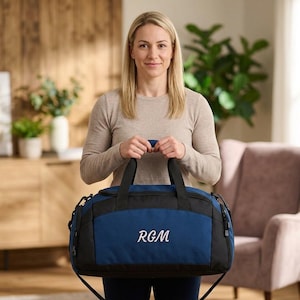 Könnte beinhalten: Eine blaue und schwarze Sporttasche mit den Initialen "RGM" in Weiß gestickt. Die Tasche hat einen Schultergurt und Griffe. Die Tasche wird von einer Person gehalten.
