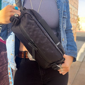 May include: A black fanny pack with a zipper closure and adjustable strap. The bag has the word "CAVET" printed on the side.