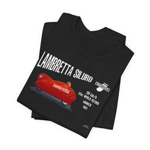 Può includere: Una t-shirt nera con una grafica del veicolo aerodinamico rosso Lambretta Siluro. Il testo riporta LAMBRETTA SILURO, INNOCENTI, 201 km/h, 125cc WORLD RECORD, MUNICH 1951. Il disegno è stampato in bianco e rosso sul davanti della maglietta.