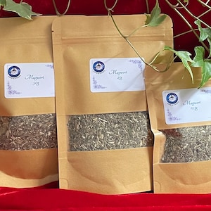 May include: Three brown paper bags with white labels that say "Mugwort" and the weight in grams. The bags are filled with dried herbs.
