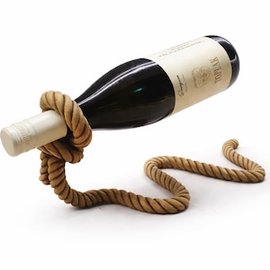 May include: A decorative wine bottle holder made of thick, beige rope. The rope is knotted to cradle the bottle, with the rest of the rope forming a curved base. A dark wine bottle with a white label is held in the holder.