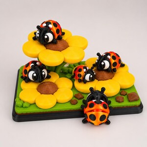 May include: A whimsical diorama featuring several ladybugs with orange and black spotted shells. The ladybugs are perched on yellow flower petals with brown centers, set against a green base. The scene is a playful, miniature garden.
