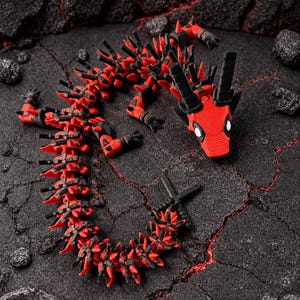 May include: A red and black articulated dragon toy, coiled on a dark, textured surface. The dragon features a detailed design with spikes and horns, and is posed as if it is slithering. The toy is made of plastic.