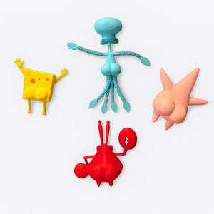 May include: Four colorful figurines of characters from a popular animated series. The characters include a yellow sponge, a blue squid, a red crab, and a pink starfish. The figures are brightly colored and stand out against the white background.